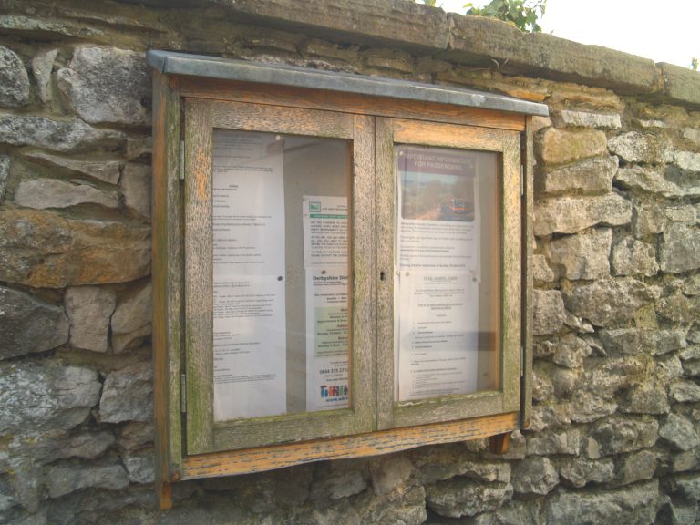 A wooden framed noticeboard attached to a stone wall.